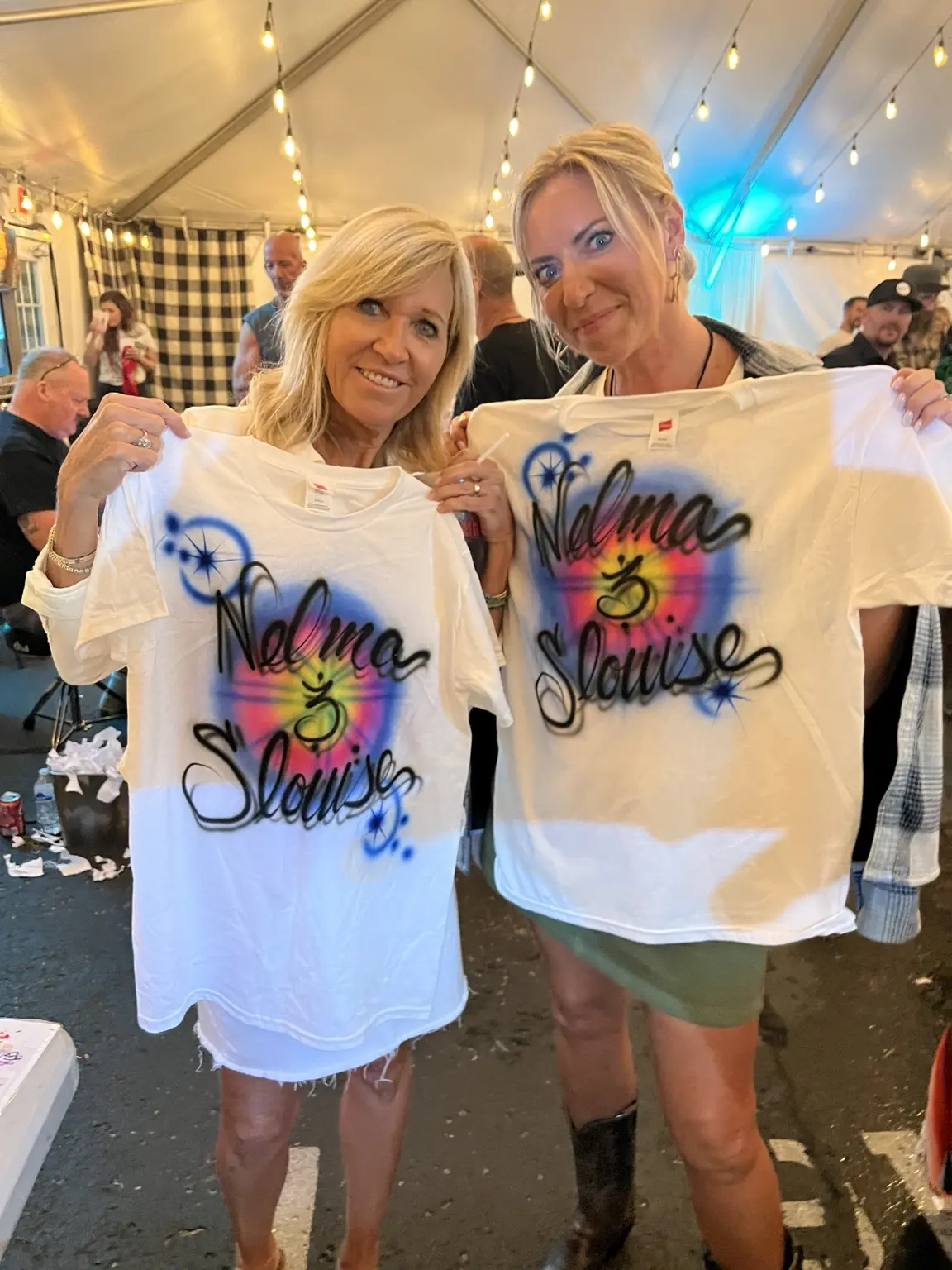 Two backstage guests displaying personalized airbrushed shirts at a Nashville music event