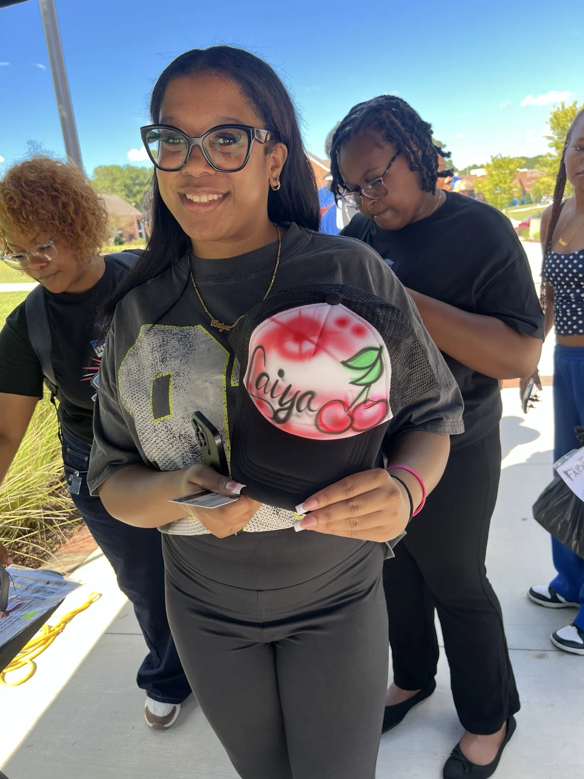 Guest holding a cherry-design airbrushed trucker hat at Fayetteville State University homecoming