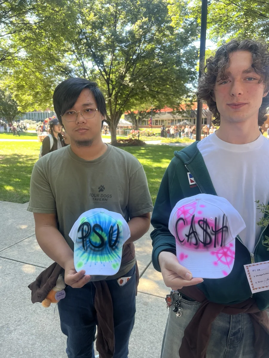 Two guests displaying blue and pink airbrushed baseball hats at Penn State