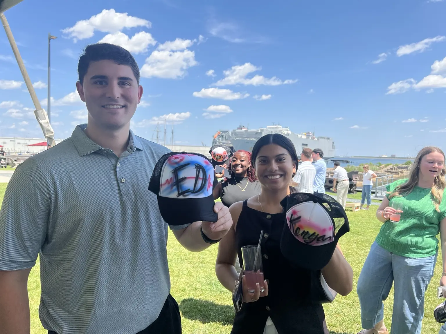 PwC guests holding custom airbrushed hats at an outdoor Baltimore corporate event