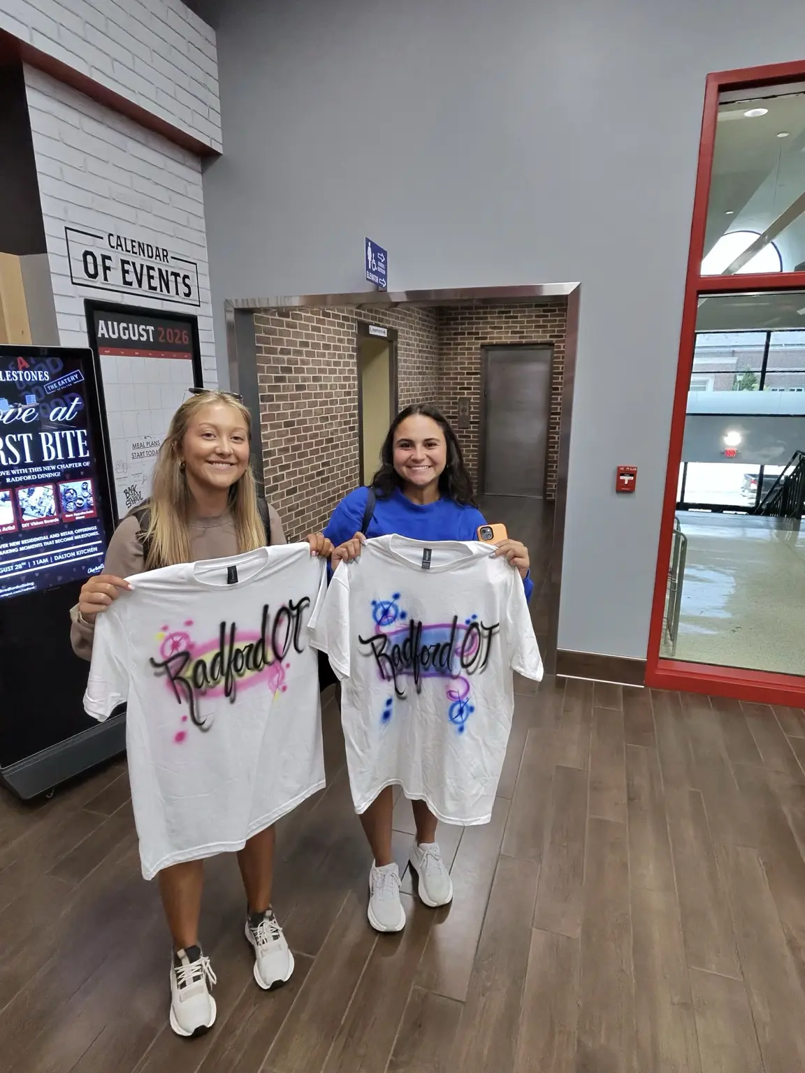 Two students holding colorful personalized airbrushed shirts at Radford University