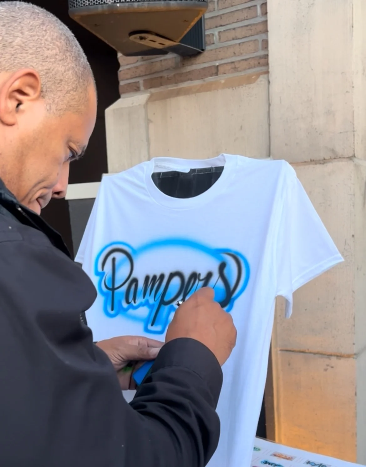 Artist painting blue Pampers lettering on a white T-shirt