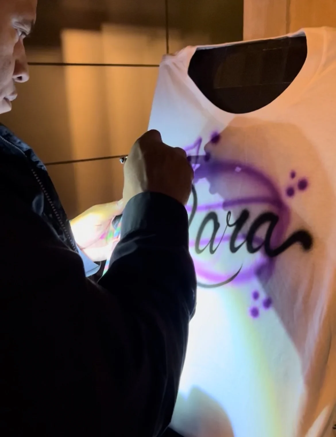 Artist painting purple lettering on a white T-shirt