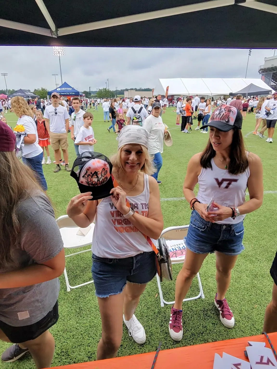 Virginia Tech guest holding a custom airbrushed Let's Go Hokies hat at Hokie Village in Blacksburg