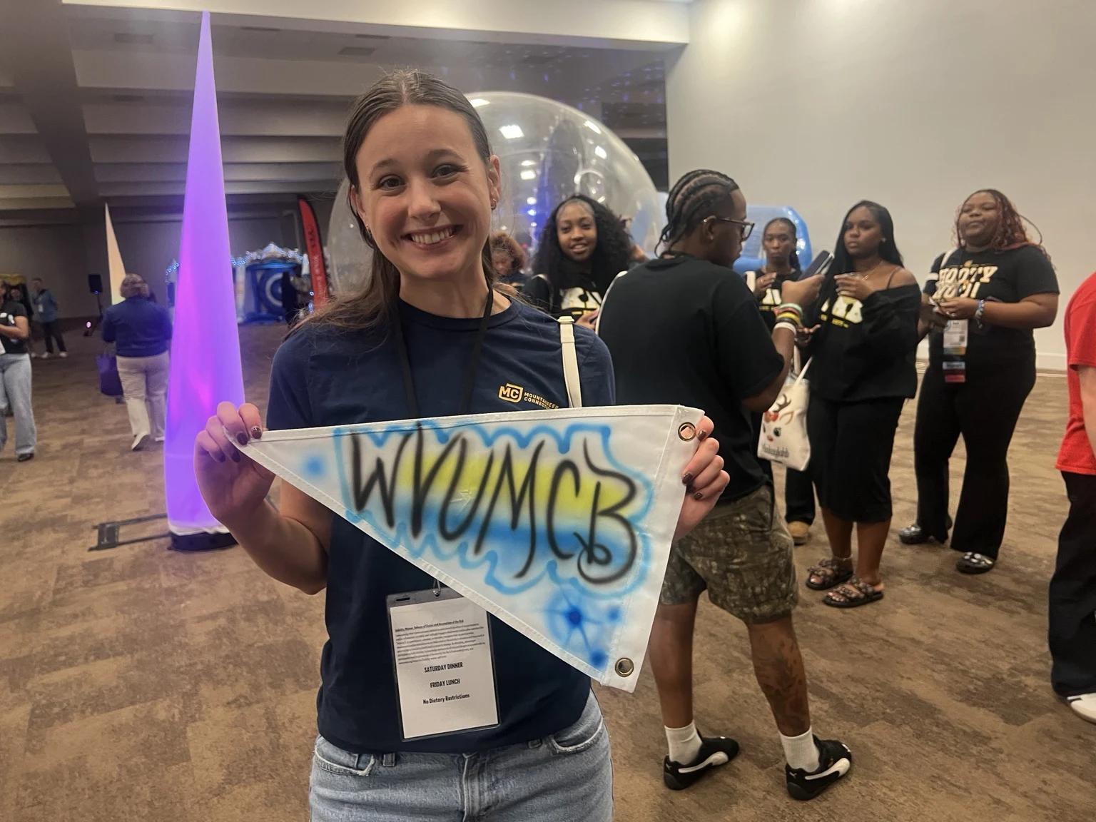 West Virginia University student holding a custom airbrushed triangular team pennant with blue and yellow accents